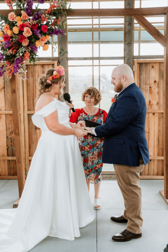 The bride and groom exchanging vows with a big garland of colourful flowers hanging overhead.