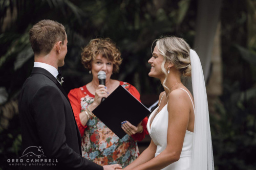 Bride, groom exchanging vows in a church with a stained glass window in the background.