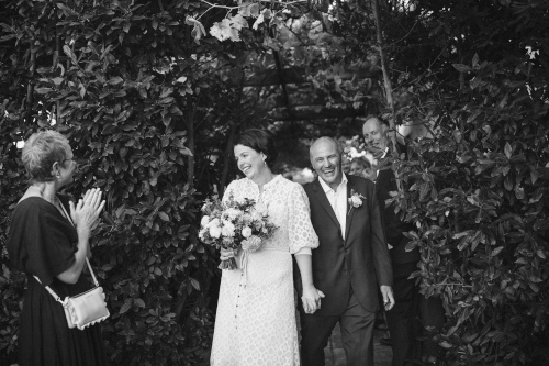 The bride and groom coming through the bush lined path.